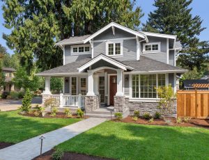 A craftsman home with gray roofing and siding has a well manicured lawn.