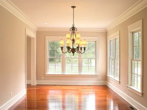 An empty living room with a chandelier and large double-hung windows.