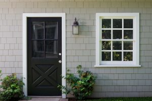 A black entry door on a home with gray shingle siding.