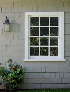 A double-hung window on a house with gray single siding.